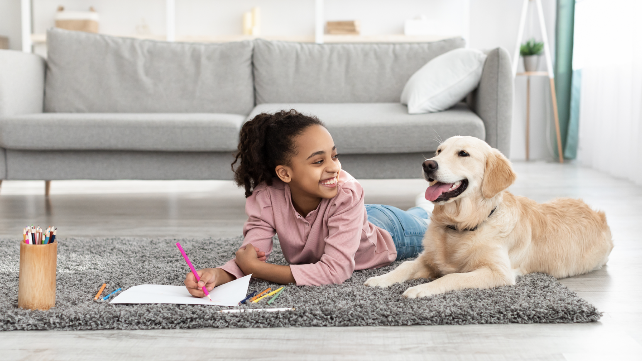 Young girl drawing while lying with her emotional support dog on a gray carpet — ESAs for children